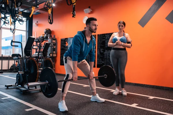 Mujer regordeta viendo a su entrenador haciendo ejercicio con la barra —  Fotos de Stock