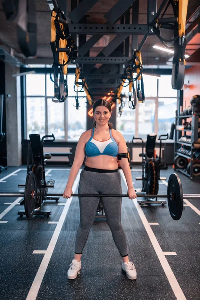 Plump kvinna håller skivstång stående i Fitness Center — Stockfoto