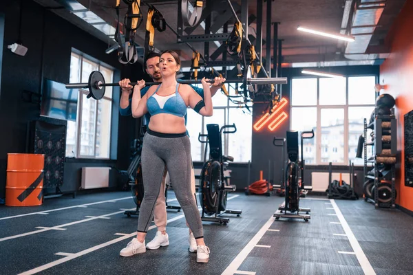 Mujer apenas respirando después de levantar la barra de pie cerca de entrenador — Foto de Stock