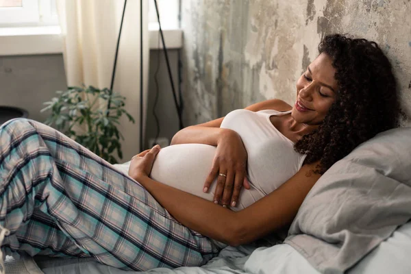 Hamile kadın karnını tutuyor ve gülümsüyor.. — Stok fotoğraf