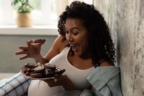 Gelukkige zwangere vrouw kraaiende eten chocolade koekjes. — Stockfoto