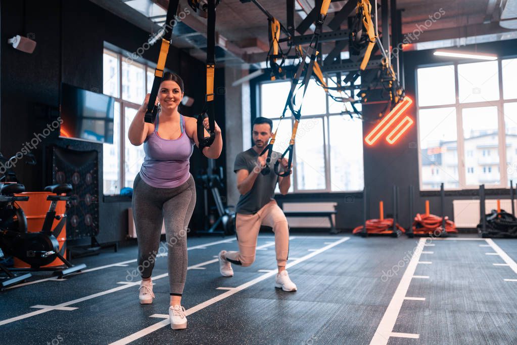 Overweight woman feeling positive while exercising with TRX
