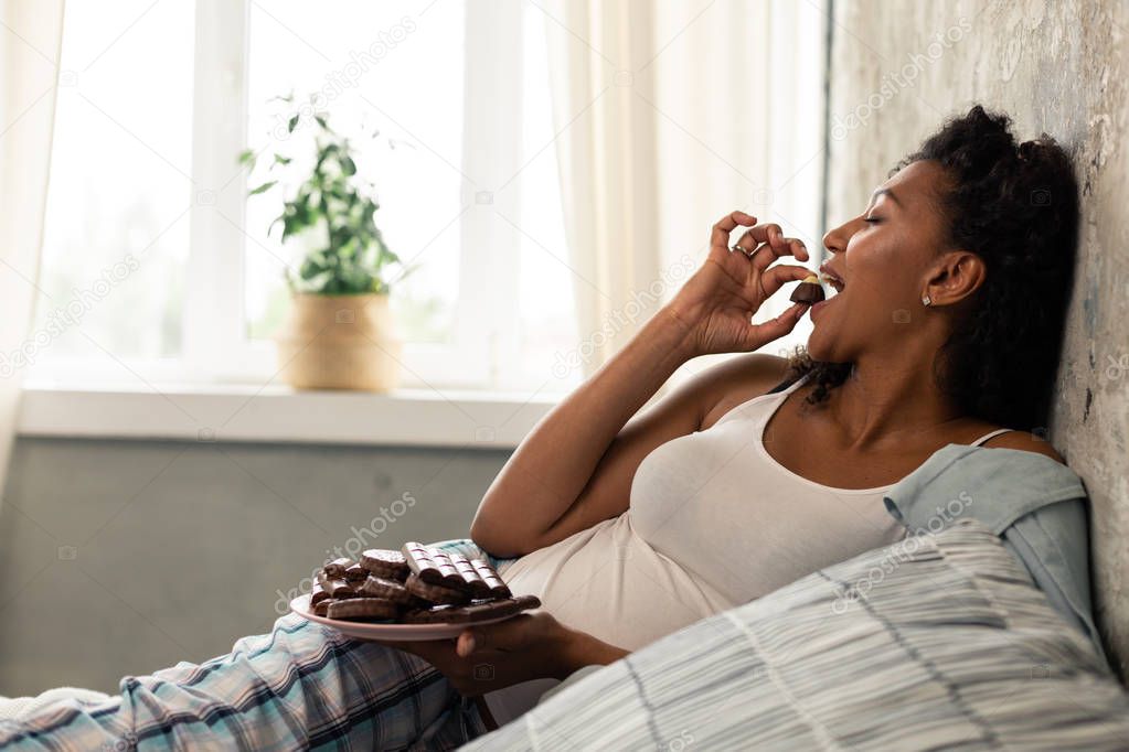 Beautiful pregnant woman eating candies in her bed.