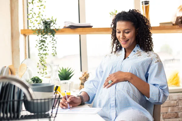 Schwangere legt Hand auf Bauch und schreibt. — Stockfoto