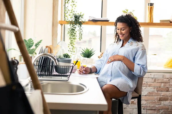 Leende gravid kvinna skriver i hennes graviditet kalender. — Stockfoto