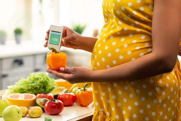 Pregnant woman measuring nitrates in a sweet pepper. — Stock Photo, Image