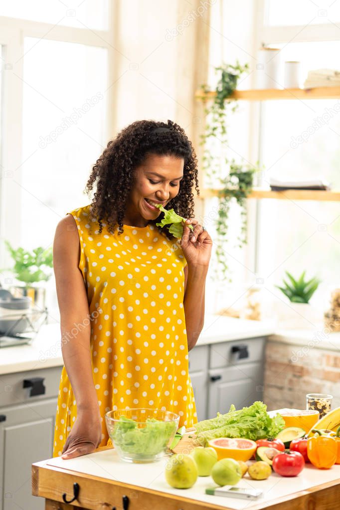 Happy pregnant woman eating lettuce in her kitchen.
