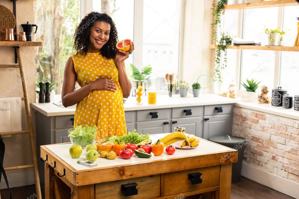 Smiling expectant mother holding a half of grapefruit.