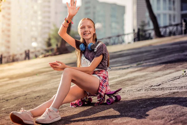 Beaming adolescente de cabelos compridos em uma camiseta acenando com a mão — Fotografia de Stock