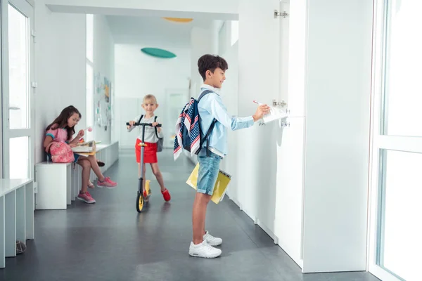 Schoolboy taking notebook from locker standing in the school corridor