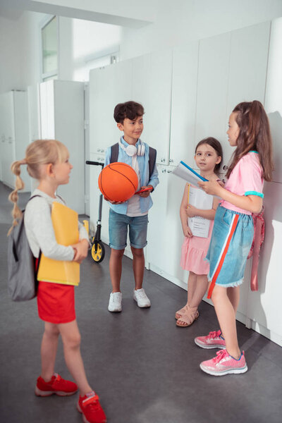 Dark-haired boy holding basketball ball speaking with girls