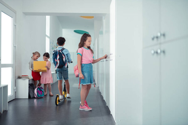 Girl wearing denim skirt and pink t-shirt standing near locker