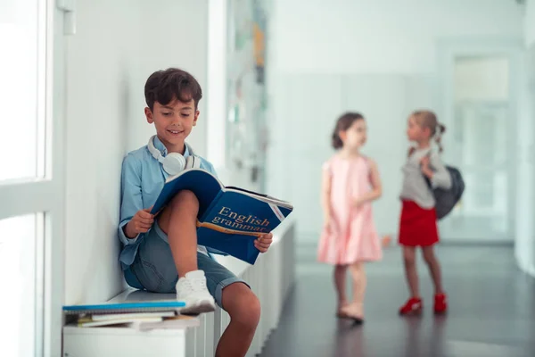 Schoolboy beyaz Sneakers oturan ve kitap okuma giyiyor — Stok fotoğraf