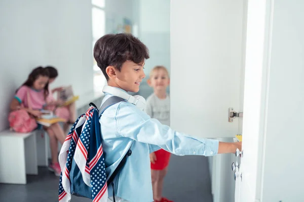 Handsome schoolboy wearing backpack standing near locker