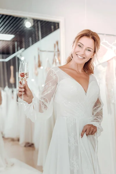 Красивая женщина пьет шампанское и примеряет свадебное платье . — стоковое фото