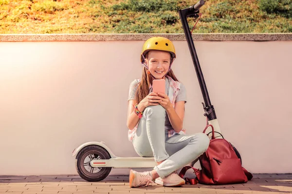 Glimlachend goed uitziende tiener meisje in lichte outfit zittend op elektronische scooter — Stockfoto