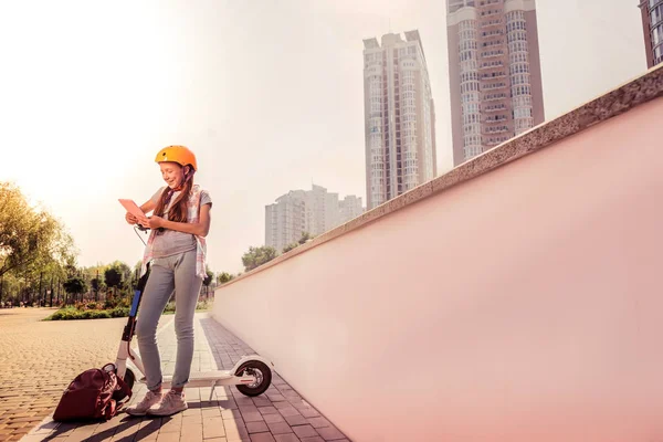 Chica flaca alegre en jeans ligeros apoyados en un scooter tranquilo —  Fotos de Stock