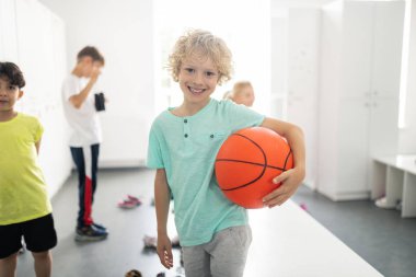 Soyunma odasında basketbol tutan gülümseyen öğrenci.