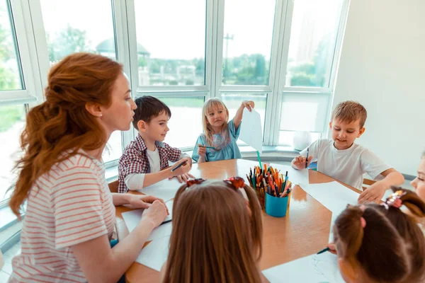 Zachwycona pozytywna dziewczyna pokazując jej rysunek dla nauczyciela — Zdjęcie stockowe