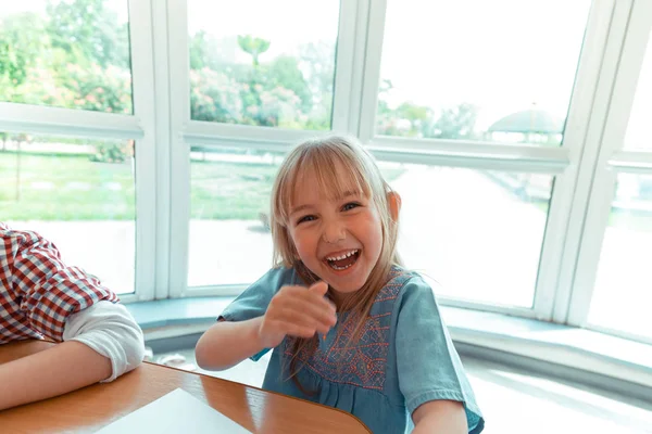 Ευτυχισμένο κορίτσι ξανθιά κάθεται στο τραπέζι — Φωτογραφία Αρχείου