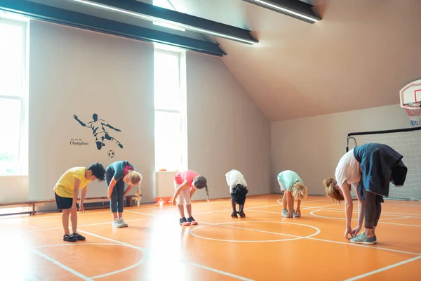 Alunos curvando-se na aula de esportes com seu treinador . — Fotografia de Stock