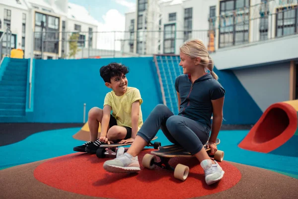 Duas crianças conversando sentadas em seus skates . — Fotografia de Stock