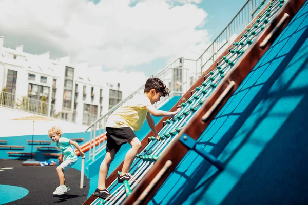 Schoolboy escalando uma escada de corda em um campo de esportes . — Fotografia de Stock
