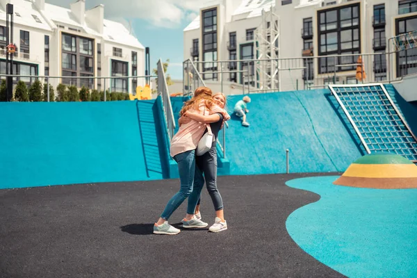 Menina alegre abraçando sua mãe apertado em um campo de esportes . — Fotografia de Stock