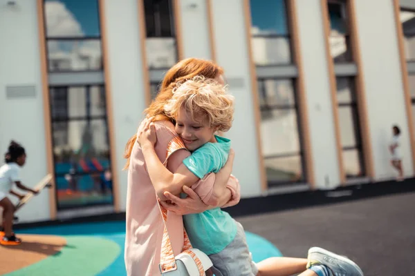 校庭でお母さんと抱き合う笑顔の少年. — ストック写真