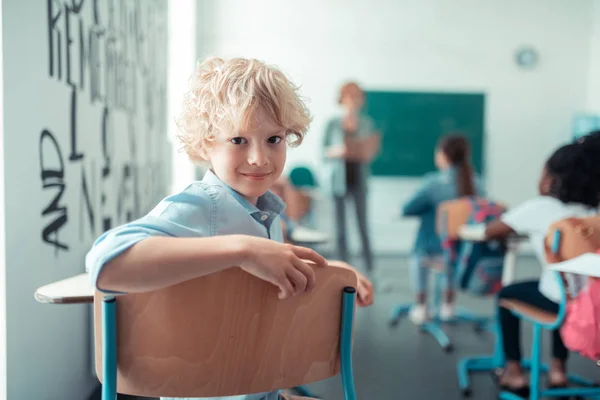 Lachende jongen keert terug zittend op zijn school Bureau. — Stockfoto