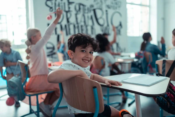 Pequeño niño sonriendo sentado en la parte trasera de la clase . — Foto de Stock