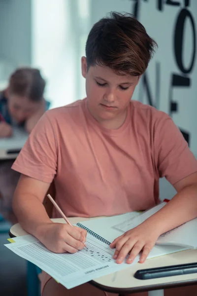 Focused pupil writing his test in a workbook. — Stock Photo, Image