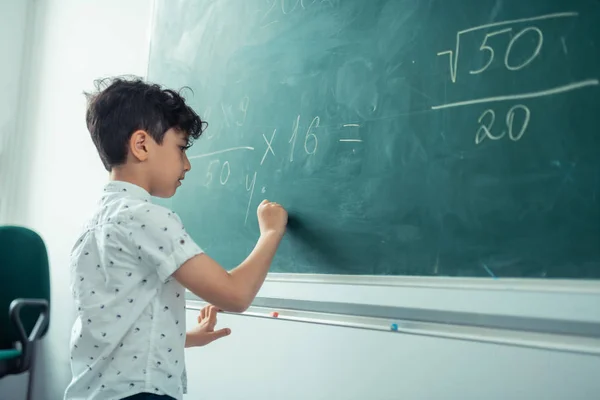 Piccolo scolaro concentrato che scrive sulla lavagna . — Foto Stock