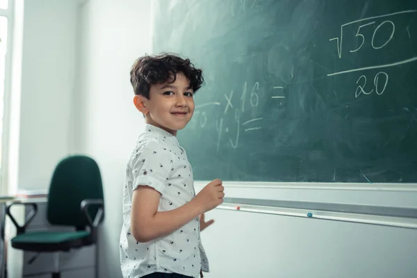 Pupil smiling standing near the blackboard with sums. — Stock Photo, Image
