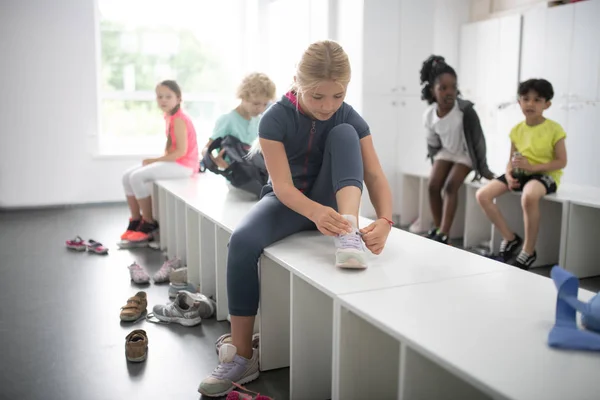 Μαθήτρια κορδονάκια τα παπούτσια της κάθονται στον πάγκο. — Φωτογραφία Αρχείου
