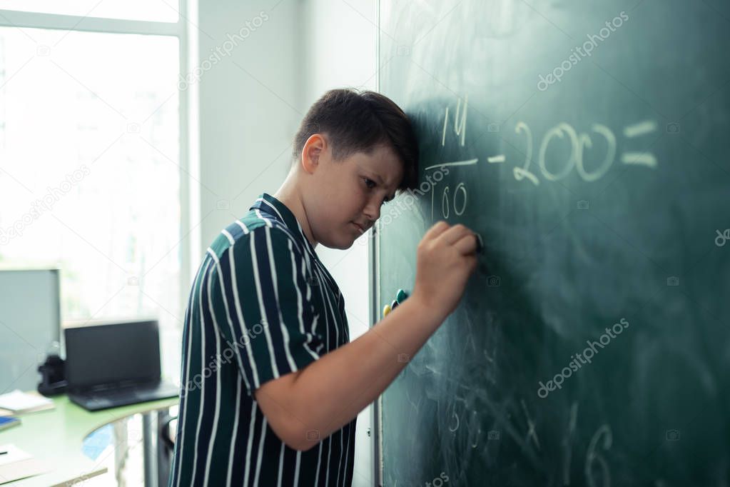 Upset pupil trying to do sums at the blackboard.