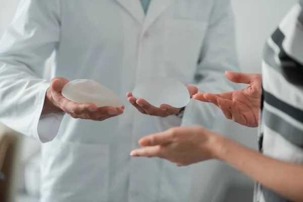 Meme için implant tutan beyaz laboratuvar önlüğü giyen plastik cerrah — Stok fotoğraf