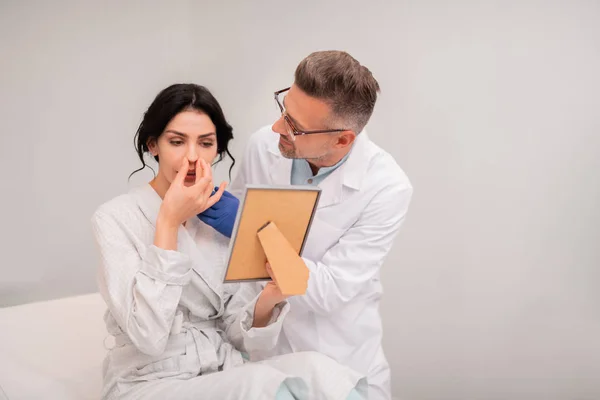 Cliente de cirujano plástico que mira en el espejo después de la cirugía nasal — Foto de Stock