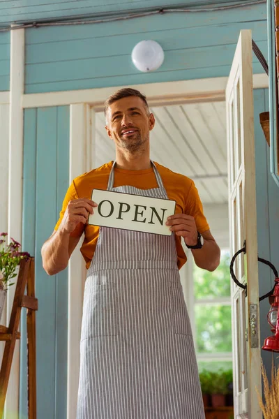 Handsome florist holding a sign with the word open. — Stock Photo, Image