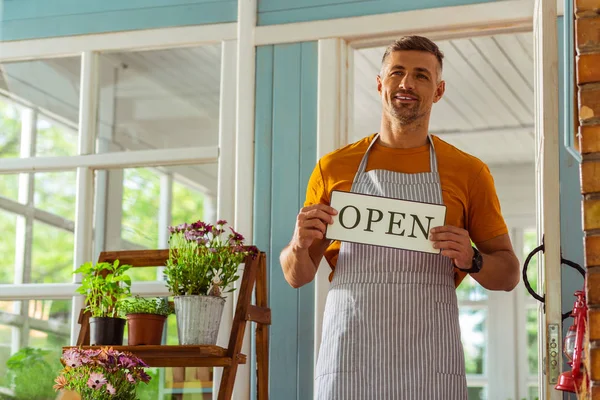 Smiling man holding an open sign near his shop. — Stock Photo, Image