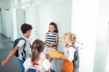 Dolapların yanında duran ve okul gününü tartışan dört çocuk