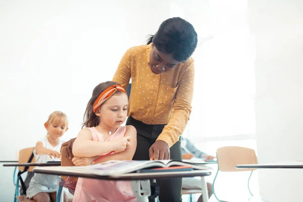 Афро-американський вчитель допомагає милою дівчинкою сидить на столі — стокове фото