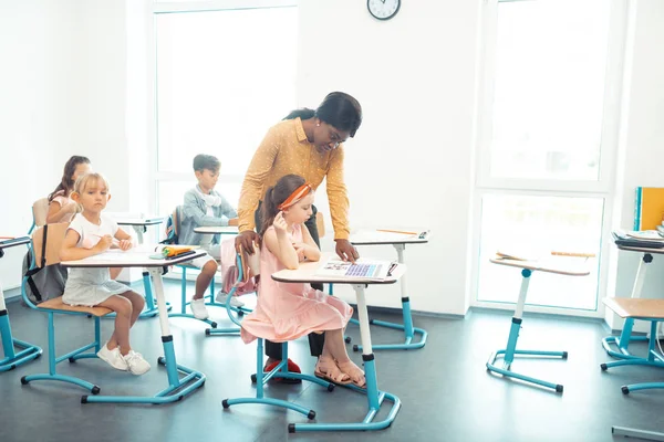 Helpful dark-skinned teacher helping children with task — Stock Photo, Image