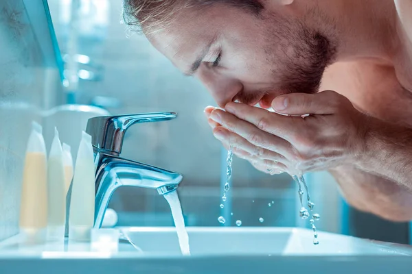 Rauhallinen unelias kaveri pesee kasvot kirkkaalla vedellä — kuvapankkivalokuva