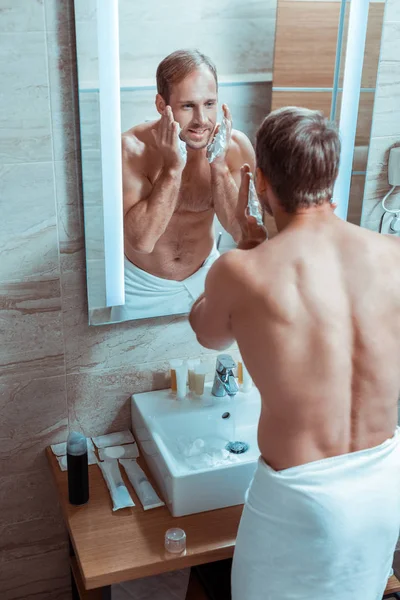 Частично голый мужчина в белом полотенце, сосредоточенный на подготовке к бритью — стоковое фото