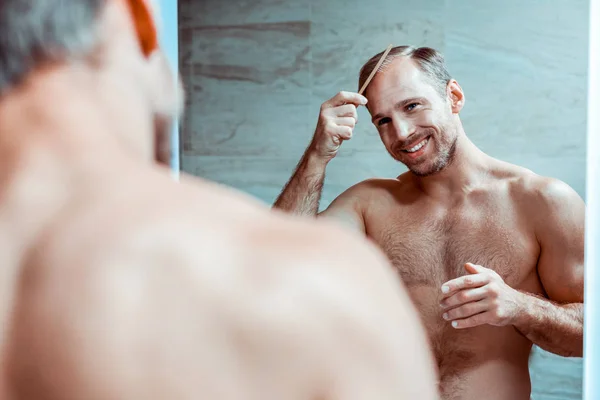 Cheerful strong man with naked torso brushing hair — Stock Photo, Image