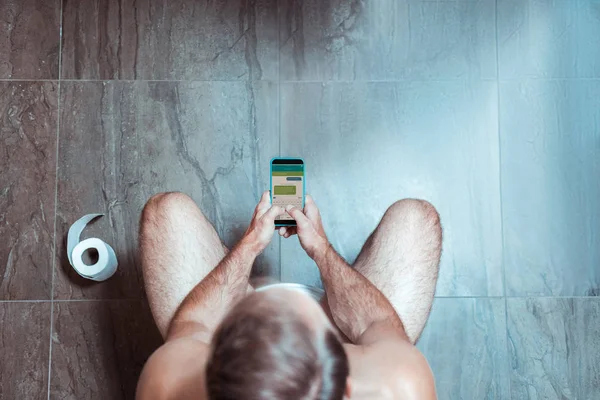 El hombre concentrado está en su teléfono mientras está sentado en el inodoro — Foto de Stock