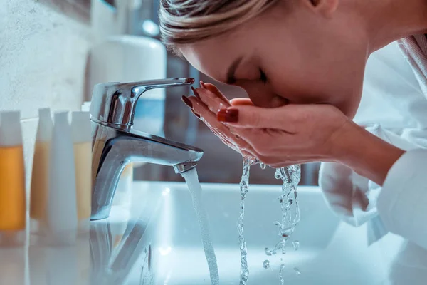 Friedliche Dame mit geschlossenen Augen, die ihr Gesicht mit klarem Wasser benetzt — Stockfoto