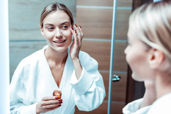 Beaming mujer joven que se aloja en el elegante cuarto de baño y llevar contenedor de vidrio —  Fotos de Stock