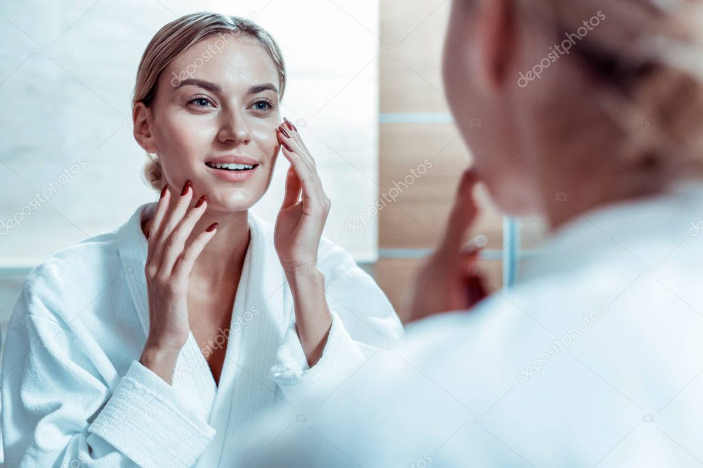 Calm blonde woman touching her face and checking state of the skin